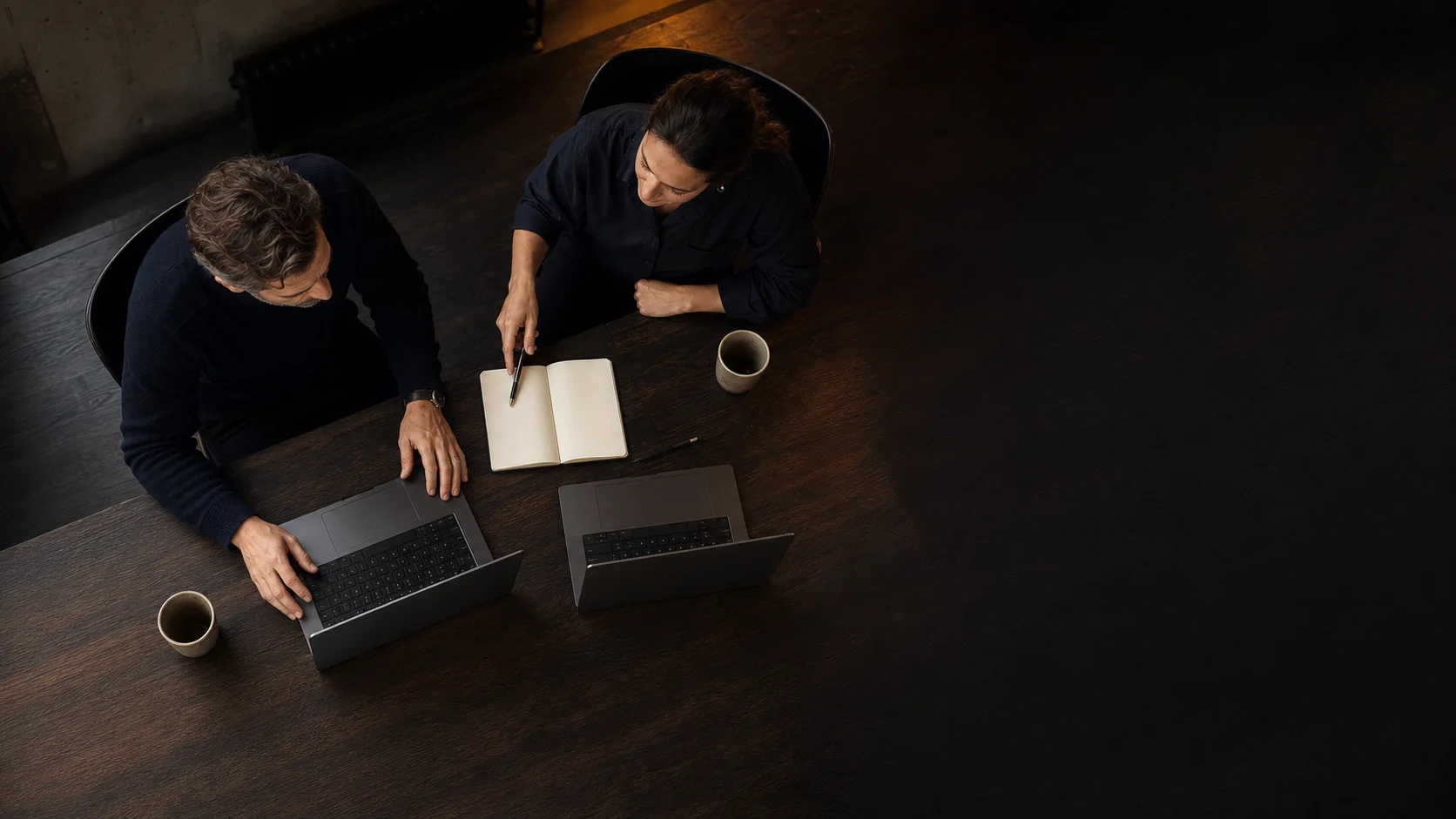Bird's-eye editorial view of two community specialists collaborating beside open laptops with hidden screens